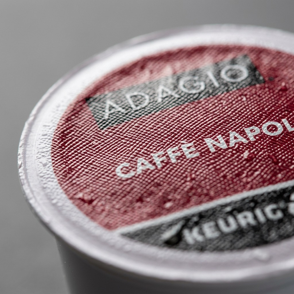 Macro detail of a Keurig Adagio Caffè Napoli K-Cup showing the textured red foil lid and branding.
