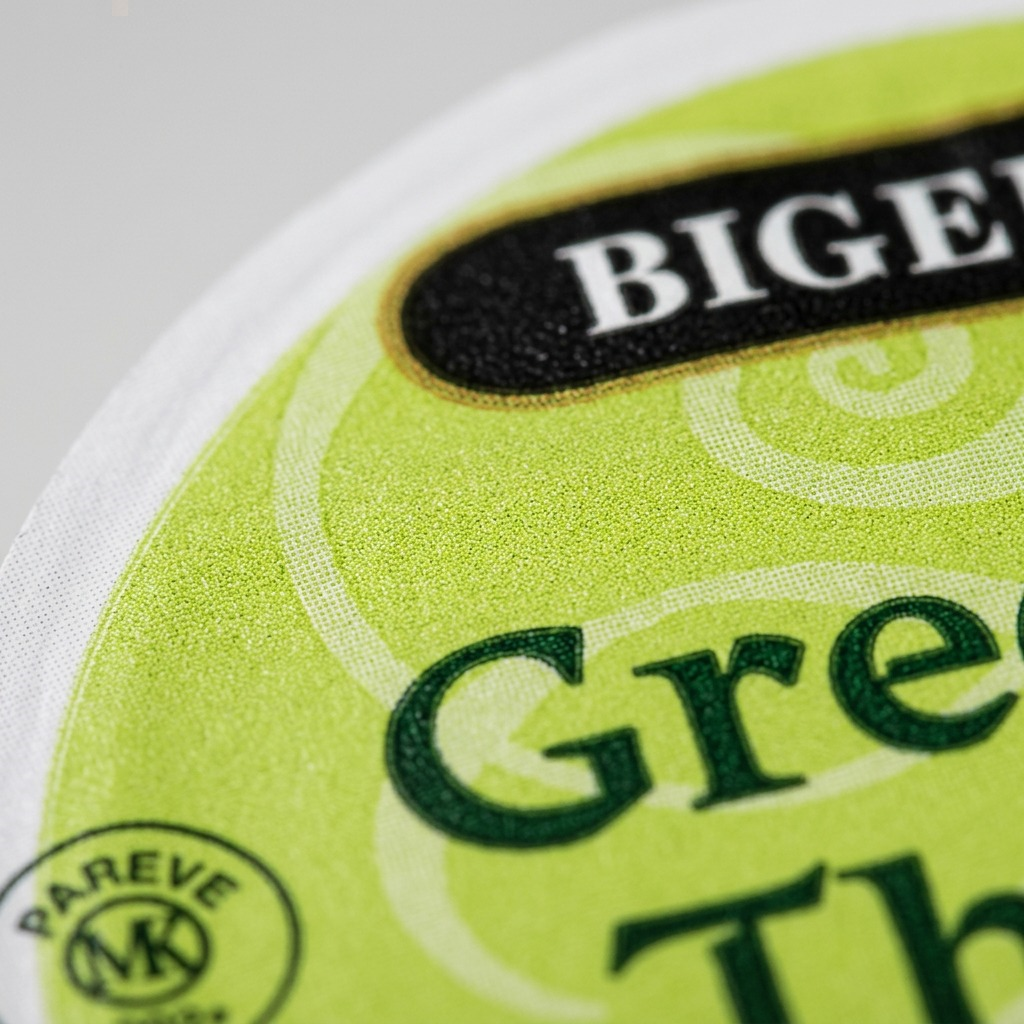Extreme close-up of a Bigelow Green Tea K-Cup lid showing the textured foil surface and print detail.