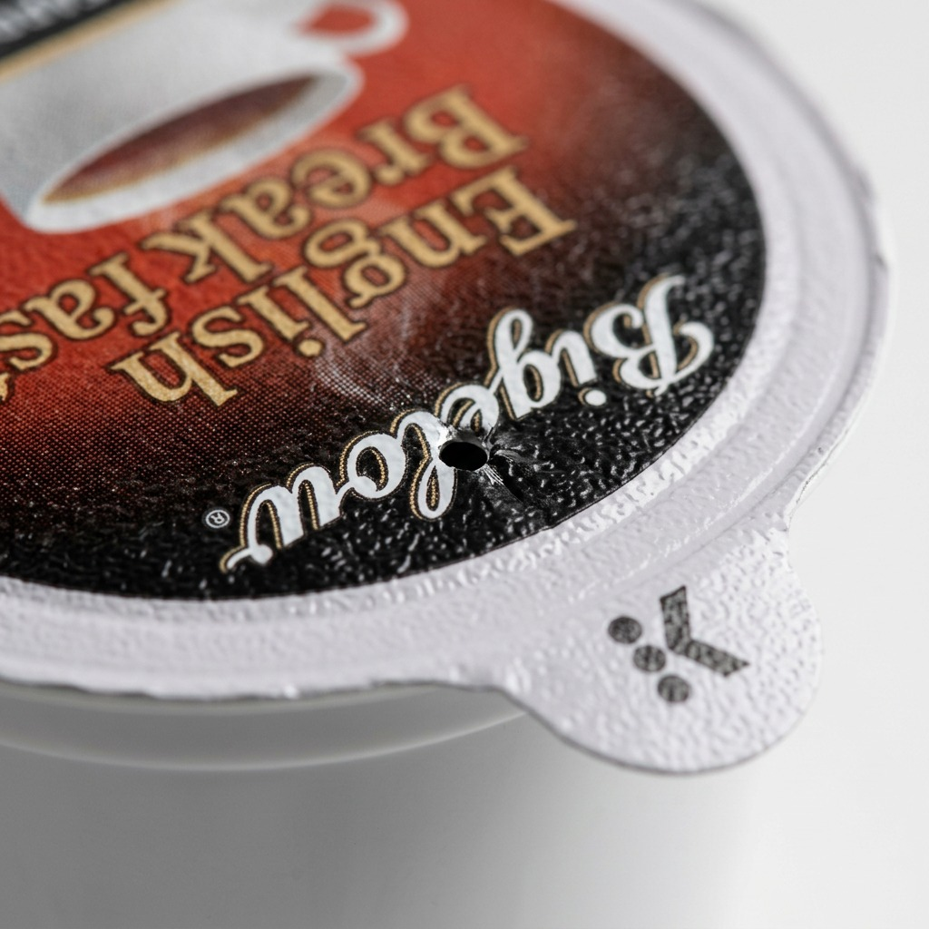 Macro detail of a punctured Bigelow English Breakfast Tea K-Cup lid showing the foil texture.